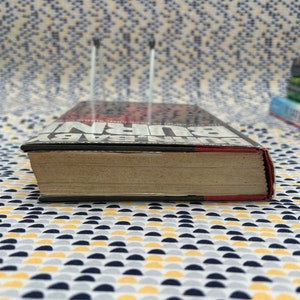 May include: A black and red paperback book with the title "BURN BABY BURN" on the spine. The book is sitting on a patterned surface.