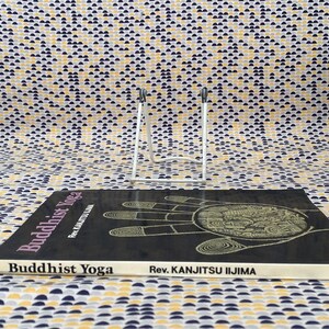May include: A black book titled "Buddhist Yoga" by Rev. Kanjitsu Iijima. The cover features a detailed illustration of a hand with a circle in the palm.