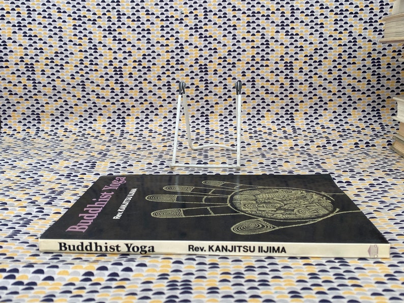 May include: A black book titled "Buddhist Yoga" by Rev. Kanjitsu Iijima. The cover features a detailed illustration of a hand with a circle in the palm.