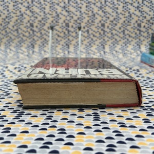 May include: A close-up of the spine of a hardcover book titled "BURN BABY BURN" by John Edgar Wideman. The book is on a patterned surface.