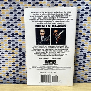 Puede incluir: Un p&oacute;ster de pel&iacute;cula para la pel&iacute;cula Men in Black, con dos hombres con trajes negros y gafas de sol. El p&oacute;ster tiene el t&iacute;tulo "Men in Black" en letras blancas grandes y el lema "Mr. Jones, Mr. Smith". El p&oacute;ster tambi&eacute;n incluye el precio de la pel&iacute;cula, US $ 5,99 y $ 7,99 CAN.
