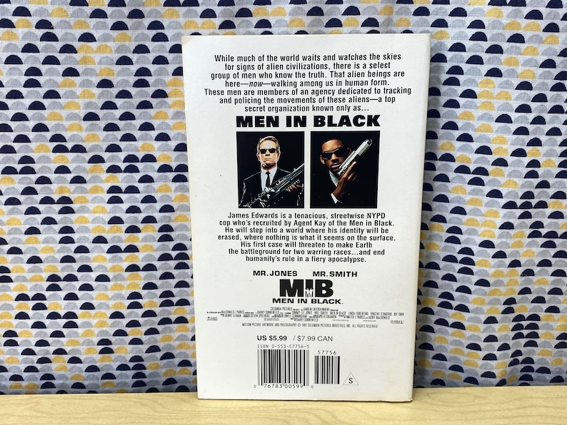 Puede incluir: Un p&oacute;ster de pel&iacute;cula para la pel&iacute;cula Men in Black, con dos hombres con trajes negros y gafas de sol. El p&oacute;ster tiene el t&iacute;tulo "Men in Black" en letras blancas grandes y el lema "Mr. Jones, Mr. Smith". El p&oacute;ster tambi&eacute;n incluye el precio de la pel&iacute;cula, US $ 5,99 y $ 7,99 CAN.