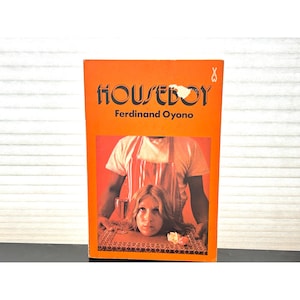 Può includere: Un libro tascabile vintage intitolato "HOUSEBOY" di Ferdinand Oyono. La copertina è arancione con testo nero e un'illustrazione grafica della testa di una persona su un tavolo. Il libro è in buone condizioni.