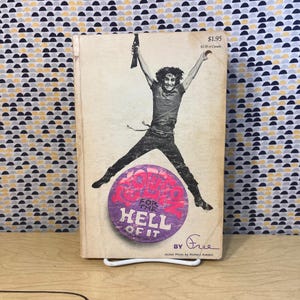May include: Vintage book cover featuring a person jumping with arms raised. The cover has a purple and pink circular design with the text "FOR THE HELL OF IT". The book is titled "FOR THE HELL OF IT" by Free.