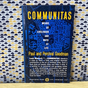 Op de afbeelding: Een vintage boekomslag met een blauwe en zwarte illustratie van een stad. De titel van het boek is "COMMUNITAS: Means of Livelihood and Ways of Life" door Paul en Percival Goodman. De boekomslag bevat ook een citaat van Lewis Mumford.
