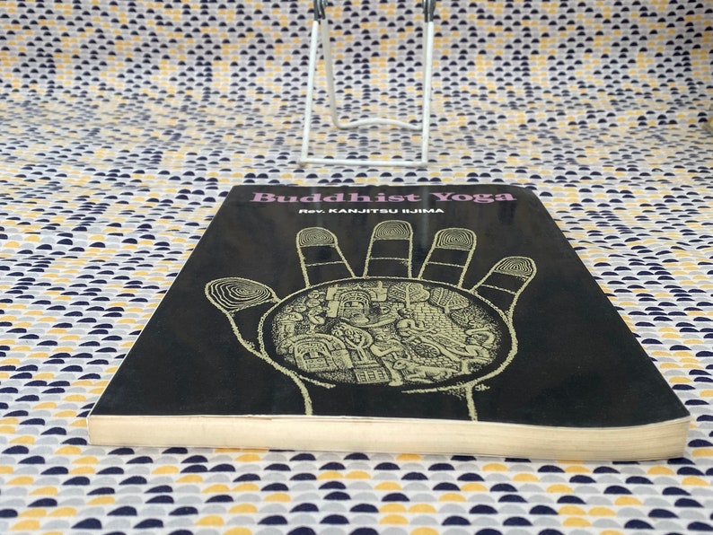 May include: A black book with the title "Buddhist Yoga" and the author "Rev. Kanjitsu Iijima". The cover features a detailed illustration of a hand with a circular design inside.