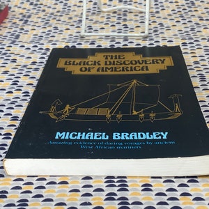 May include: A hardcover book titled "The Black Discovery of America" by Michael Bradley. The cover is black with gold lettering and a drawing of a boat. The book's subtitle reads "Amazing evidence of daring voyages by ancient West African mariners."