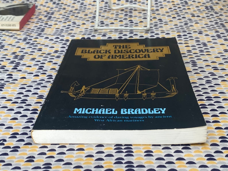 May include: A hardcover book titled "The Black Discovery of America" by Michael Bradley. The cover is black with gold lettering and a drawing of a boat. The book's subtitle reads "Amazing evidence of daring voyages by ancient West African mariners."