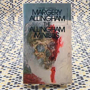 Puede incluir: Una taza de cerámica blanca con asa negra y el texto "But First, Coffee" en negrita negra. La taza se encuentra sobre un fondo borroso, sugiriendo un ambiente acogedor.