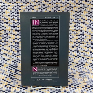 Op de afbeelding: Een zwart-witte boekomslag met de titel "Politics/Int'l" en de naam van de auteur "Noam Chomsky". De boekomslag bevat een korte beschrijving van de inhoud van het boek, inclusief een samenvatting van de lezingen en de achtergrond van de auteur.