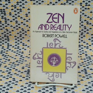 May include: A vintage paperback book titled "Zen and Reality: An Approach to Sanity and Happiness on a Non-Sectarian Basis" by Robert Powell. The cover features a yellow square with purple Sanskrit text and a purple circle with a scale and a figure.