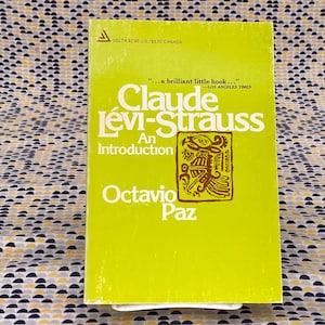 Op de afbeelding: Een geel paperback boek met de titel "Claude Lévi-Strauss Een Inleiding" door Octavio Paz. De omslag van het boek heeft een bruine en gele illustratie van een gestileerde vogel.