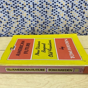 May include: A yellow and red book titled "The American Future: New Visions Beyond Old Frontiers" by Tom Hayden. The book is published by South End Press.
