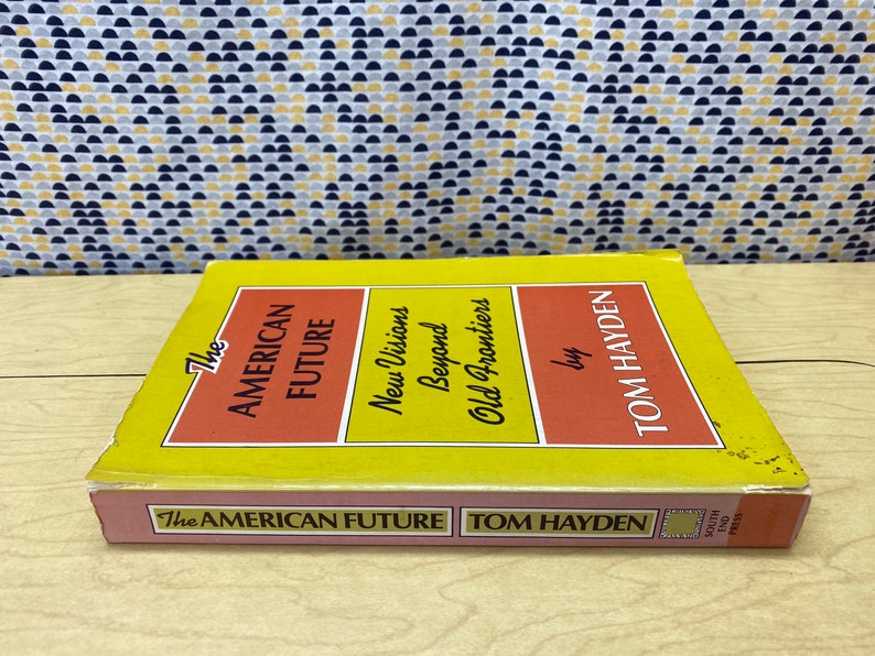 May include: A yellow and red book titled "The American Future: New Visions Beyond Old Frontiers" by Tom Hayden. The book is published by South End Press.