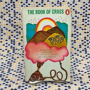 Può includere: Un libro tascabile vintage intitolato "The Book of Grass: An Anthology of Indian Hemp" con una copertina psichedelica che presenta un arcobaleno, montagne e un narghilè.