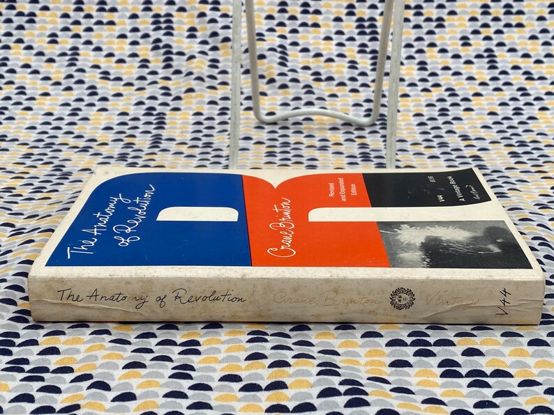Puede incluir: Un libro de bolsillo vintage titulado "The Anatomy of Revolution" de Crane Brinton. La portada es blanca con un dise&ntilde;o azul y rojo. El libro forma parte de una serie llamada "Vintage" y tiene el n&uacute;mero "V44" en el lomo.