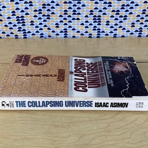 May include: A white paperback book titled "The Collapsing Universe" by Isaac Asimov. The cover features a red and white graphic of a collapsing star with a black background.