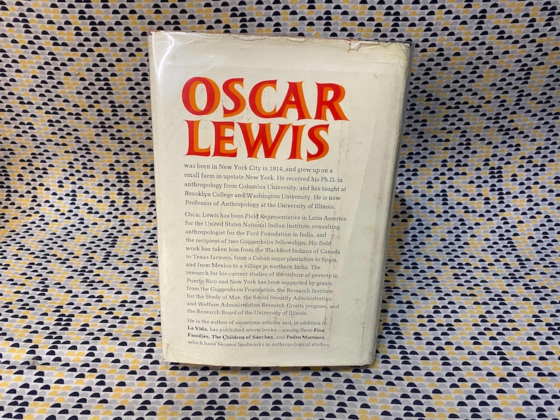 Op de afbeelding: Een witte boekomslag met de titel "Oscar Lewis" in rode en oranje letters. De tekst beschrijft Lewis' leven en carri&egrave;re als antropoloog.