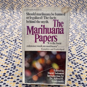 Può includere: Libro tascabile vintage intitolato "The Marihuana Papers". La copertina presenta il titolo in viola, con la domanda "La marijuana dovrebbe essere vietata o legalizzata?" e il testo "È l'opera di riferimento di base sulla marijuana". Completo e integrale.
