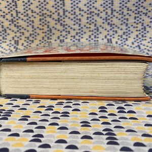 Op de afbeelding: Close-up van de rug van een hardcover boek met een zwart, oranje en wit gestreepte omslag. Het boek ligt op een gepatroneerd oppervlak.