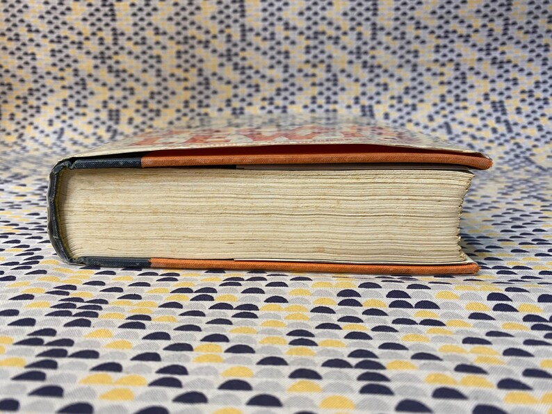 Op de afbeelding: Close-up van de rug van een hardcover boek met een zwart, oranje en wit gestreepte omslag. Het boek ligt op een gepatroneerd oppervlak.
