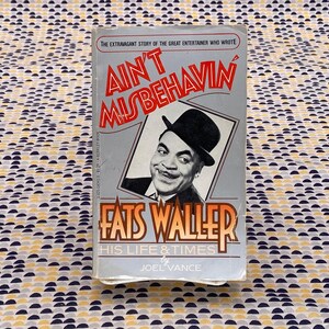 Puede incluir: Una portada de libro vintage con una foto en blanco y negro de Fats Waller, un famoso músico de jazz. El título del libro es "Ain't Misbehavin'" y el subtítulo es "His Life & Times by Joel Vance".