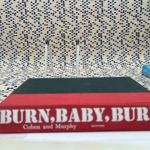 May include: A red hardcover book with the title "BURN, BABY, BURN!" in white letters. The author's names, "Cohen and Murphy", are printed in white below the title.