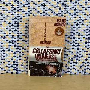 May include: A paperback book titled "The Collapsing Universe: The Story of Black Holes" by Isaac Asimov. The book cover features a black and white image of a galaxy with a bright, white star in the center. The book is part of the "The Mystery of Time and Space" series.