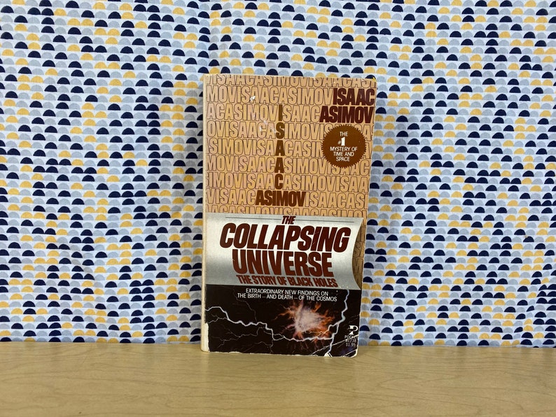 May include: A paperback book titled "The Collapsing Universe: The Story of Black Holes" by Isaac Asimov. The book cover features a black and white image of a galaxy with a bright, white star in the center. The book is part of the "The Mystery of Time and Space" series.