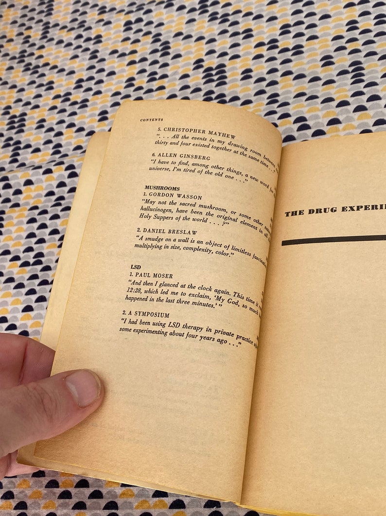 May include: A close-up of a book page with the title "The Drug Experience" and a list of contents including "Mushrooms", "LSD", and "A Symposium".