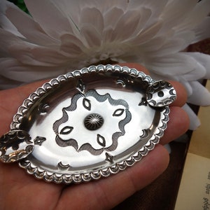 Puede incluir: Un plato de plata ovalado con un diseño decorativo. El plato tiene un centro elevado con un patrón de estrella y un borde festoneado.