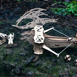 May include: A wooden model of a dragon with three heads, a crossbow, and four figures. The dragon is made of laser-cut wood and has a detailed design. The crossbow is also made of wood and has a string attached to it. The figures are small and are also made of wood.