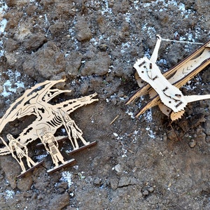 May include: A wooden dragon figurine with three figures standing in front of it. The dragon is facing a wooden catapult with a string attached to it.