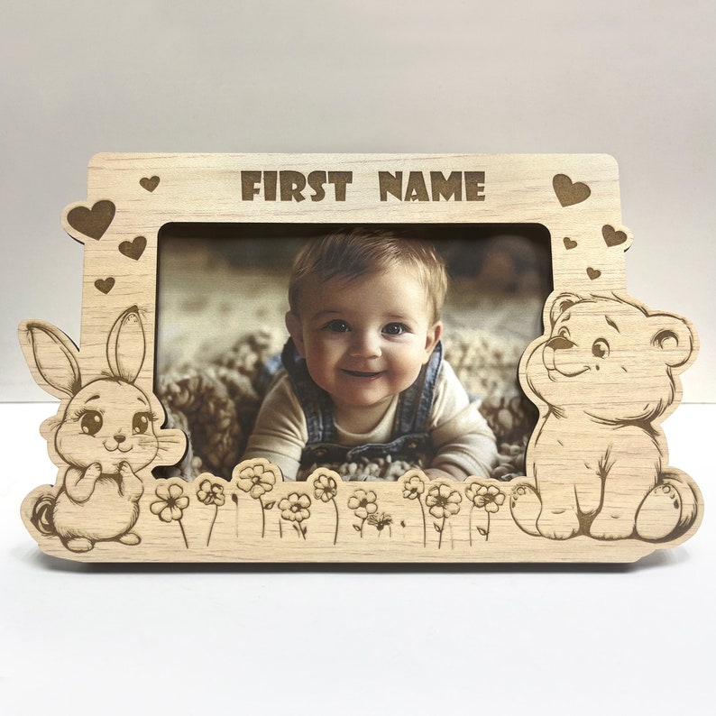 May include: A wooden photo frame with a cutout of a bunny and a bear on either side. The frame has a space for a photo and the words "FIRST NAME" are engraved at the top.
