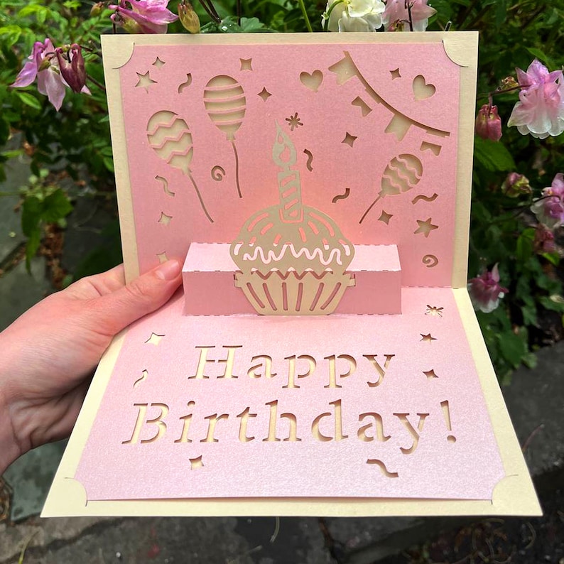 3D pop up Birthday card with a laser cut cupcake and balloons design. Handmade pink paper card with a "Happy Birthday" greeting, created from an SVG cutting file.
