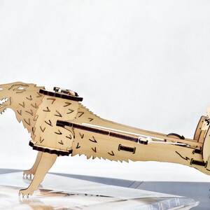May include: A wooden model of a wolf, with a detailed design of fur and a snarling expression. The model is made of light brown wood and is assembled in a standing position.