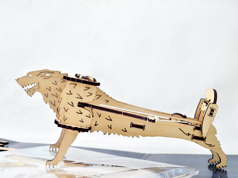 May include: A wooden model of a wolf, with a detailed design of fur and a snarling expression. The model is made of light brown wood and is assembled in a standing position.
