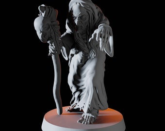 May include: A gray figurine of a wizened witch, draped in a hooded robe, holding a staff topped with a skull. The witch stands on a circular base, with a detailed, aged appearance. The lighting creates shadows.