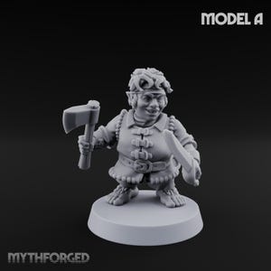 May include: A gray miniature figure of a fantasy character, holding an axe and a knife. The figure is wearing a tunic with a belt and has pointed ears. The base is round. The text "MODEL A" is at the top right. The text "MYTHFORGED" is at the bottom left.