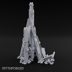May include: A light grey miniature terrain piece featuring a tall, vertical wooden post structure reinforced with rope bindings and metal plates. A small shield is attached to the side, and a broken wooden crate lies at the base. The text MYTHFORGED is visible.