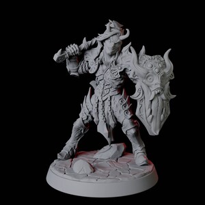 Puede incluir: Figura gris de un guerrero con armadura ornamentada, sosteniendo una espada y un escudo. El escudo presenta un diseño de cara de monstruo. El guerrero está de pie sobre una base de piedra agrietada. La figura tiene una expresión amenazante.
