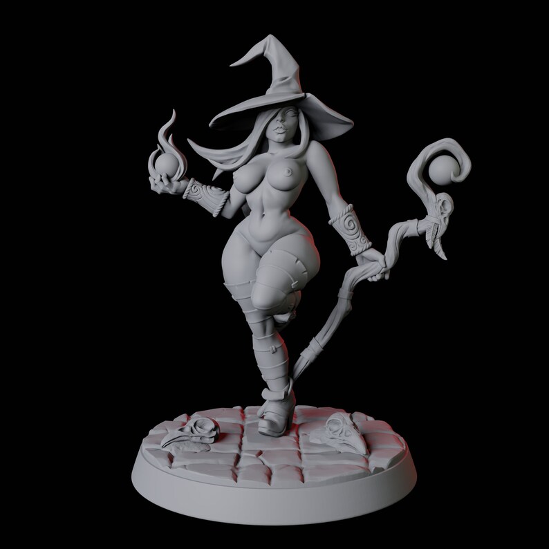 May include: A gray, nude, female figurine of a witch wearing a pointed hat and holding a staff with a sphere on top. The figurine is standing on a round base with a textured surface.