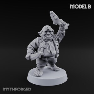 May include: A gray figurine of a stout character holding a fish aloft and a knife. The figure is wearing a vest, shirt, and tie. The base is round. The text "MODEL B" is at the top right. The text "MYTHFORGED" is at the bottom.