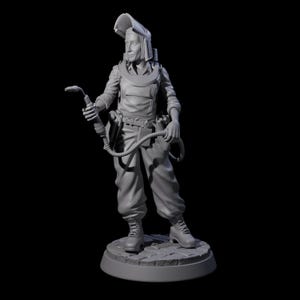 May include: A gray figurine of a welder, wearing a welding helmet, protective clothing, and work boots. The figure is holding a welding torch and hose. The figurine is standing on a circular base with a cobblestone pattern.