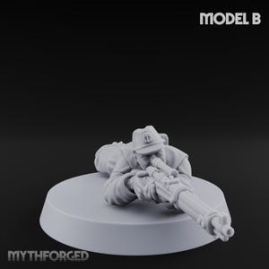 Peut inclure: Figurine miniature grise d'un soldat en position couchée, visant avec un fusil à lunette. Le soldat porte un chapeau et un uniforme. La base est un cercle gris clair. Le texte "MODEL B" est en haut à droite. Le mot "MYTHFORGED" est en bas.