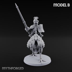 Könnte beinhalten: Graue Miniaturfigur eines Ritters, der auf einem großen Vogel reitet und einen Speer und einen Schild hält. Die Figur steht auf einem runden Sockel. Der Text "MODEL B" befindet sich in der oberen rechten Ecke und "MYTHFORGED" unten.