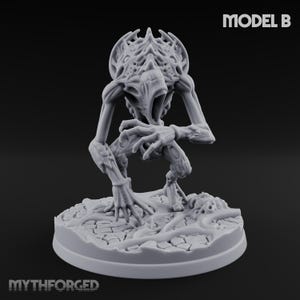May include: A grey miniature figure of a creature with an open mouth and detailed head. The figure is on a textured base, with the text "MODEL B" and "MYTHFORGED" visible.