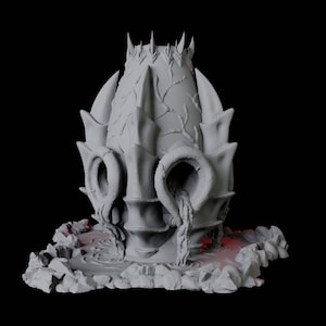 May include: A grey, 3D printed, dragon egg sculpture with a textured surface and a crown of spikes on top. The egg is resting on a base of grey, rocky terrain.