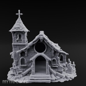 Puede incluir: Un edificio de iglesia en miniatura de color gris con un campanario alto coronado por una cruz, una entrada central arqueada, una ventana circular y paredes con textura de piedra. Incluye lápidas circundantes y el texto MYTHFORGED.