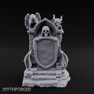 May include: A light gray resin miniature featuring a central skull figure holding a blank shield, flanked by a winged angel and a horned demon on a stone-like base. The text MYTHFORGED is visible at the bottom left of this detailed gaming figurine.